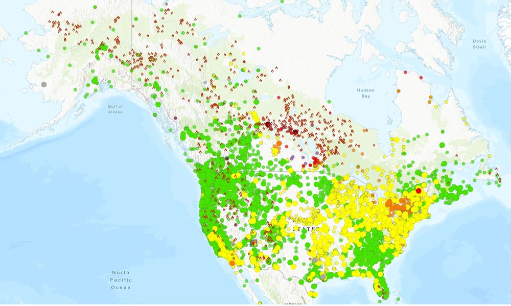 Map of North America showing active wildfires (marked with red flame icons) concentrated in western Canada and parts of the western U.S. Colored circles indicate current air quality: green (good), yellow (moderate), orange (unhealthy for sensitive groups), and red/purple (unhealthy/hazardous), with poor air quality across the central and eastern U.S., especially around the Great Lakes and Ohio Valley.
