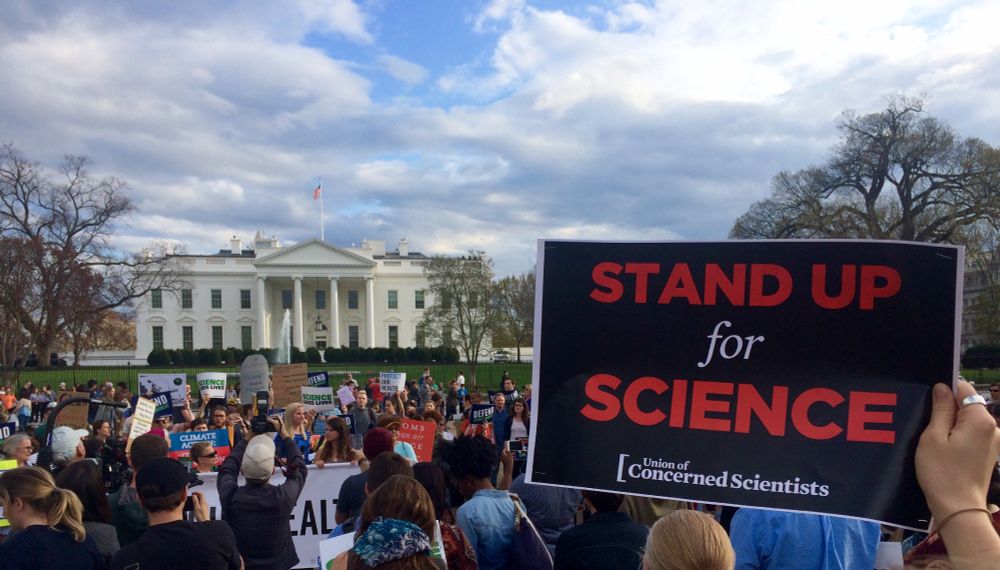 Picture of scientists in front of the White House holding a sign "Stand Up for Science"