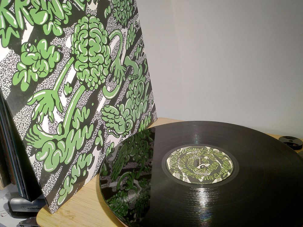 A green record sleeve propped up next to a record on a turntable 