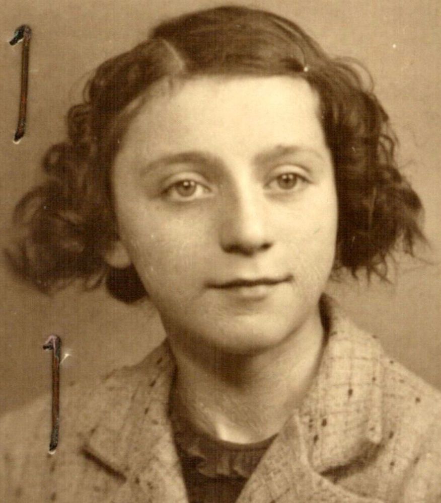 Vintage portrait of a girl, featuring her face looking directly at the camera with a neutral expression. She wears a textured coat and her mid-length hair is styled around her face.