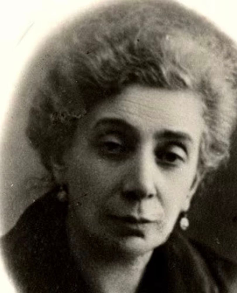 A black and white portrait of a mature woman with curly hair, looking slightly away from the camera with an expression of contemplation.