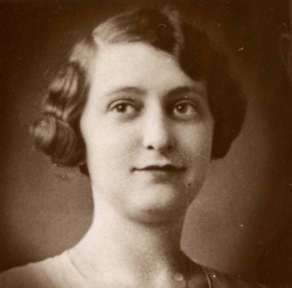 Vintage portrait of a woman with a soft smile, featuring styled hair and delicate facial features.