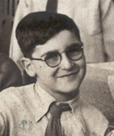 Black and white photo of a young boy wearing glasses and a tie, smiling at the camera.
