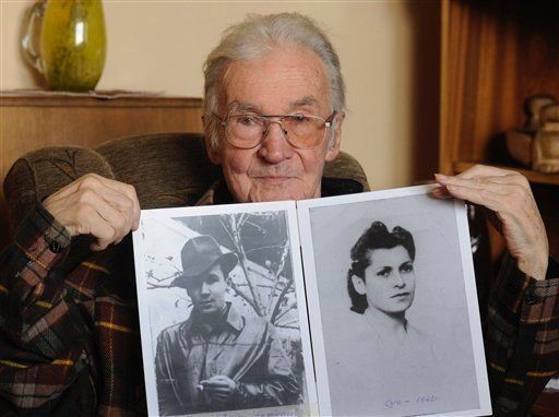 An elderly individual holding two black and white photographs, one of a young person in a coat and a hat and the other of a young woman with curly hair.