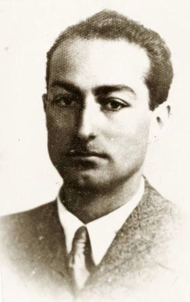 A black-and-white portrait of a young man with short, neatly combed hair. He is dressed in a formal suit and tie, and his expression is serious as he looks directly at the camera. The photograph has a vintage feel, likely taken in the early to mid-20th century.