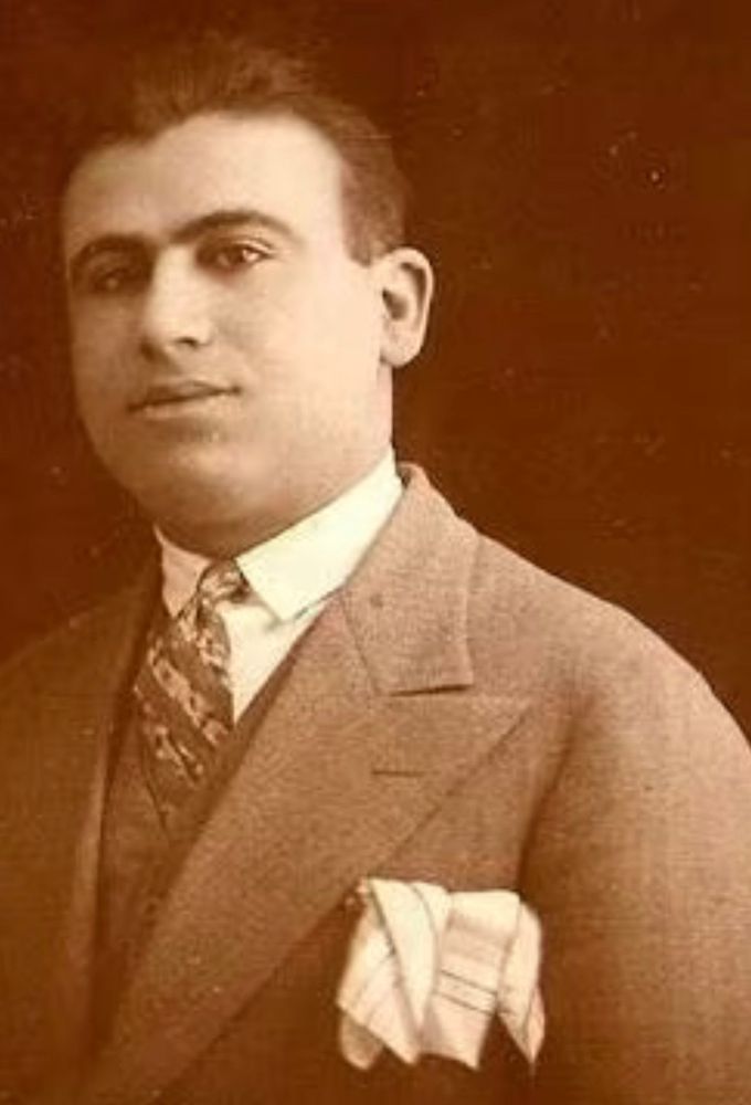 Portrait of a person from the early 20th century, wearing a formal suit and a patterned tie, posing against a plain background.