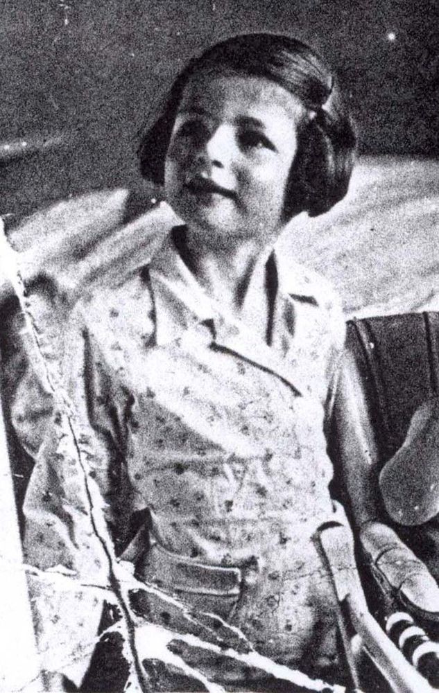 A vintage, grainy black-and-white photo of a smiling cgirl wearing a patterned dress