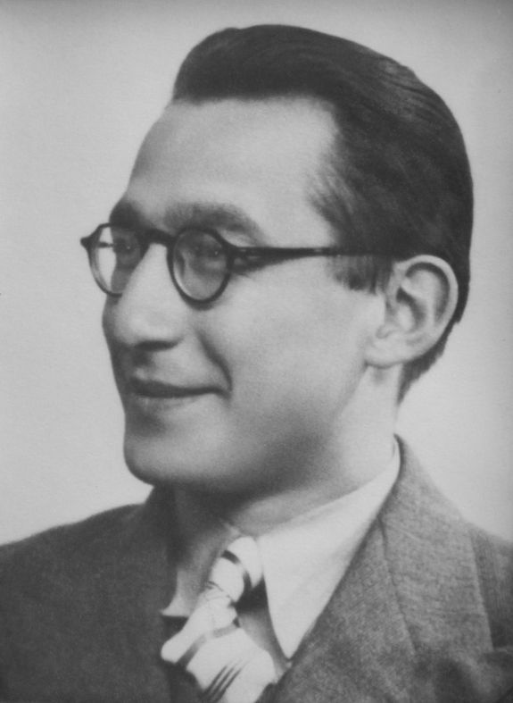 A portrait photo of a man in a suit with short dark hair and glasses.