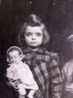 Vintage black and white photo of a girl holding a small doll, wearing a plaid dress.