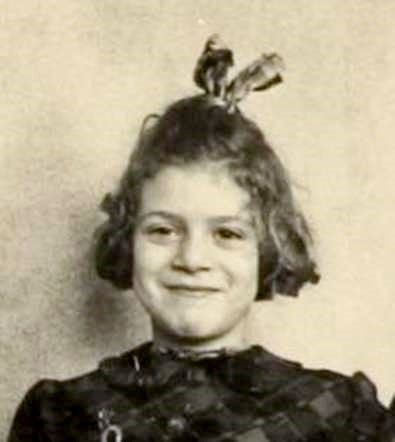 A vintage black and white photo showing a smiling girl with a small ribbon on top of their head.