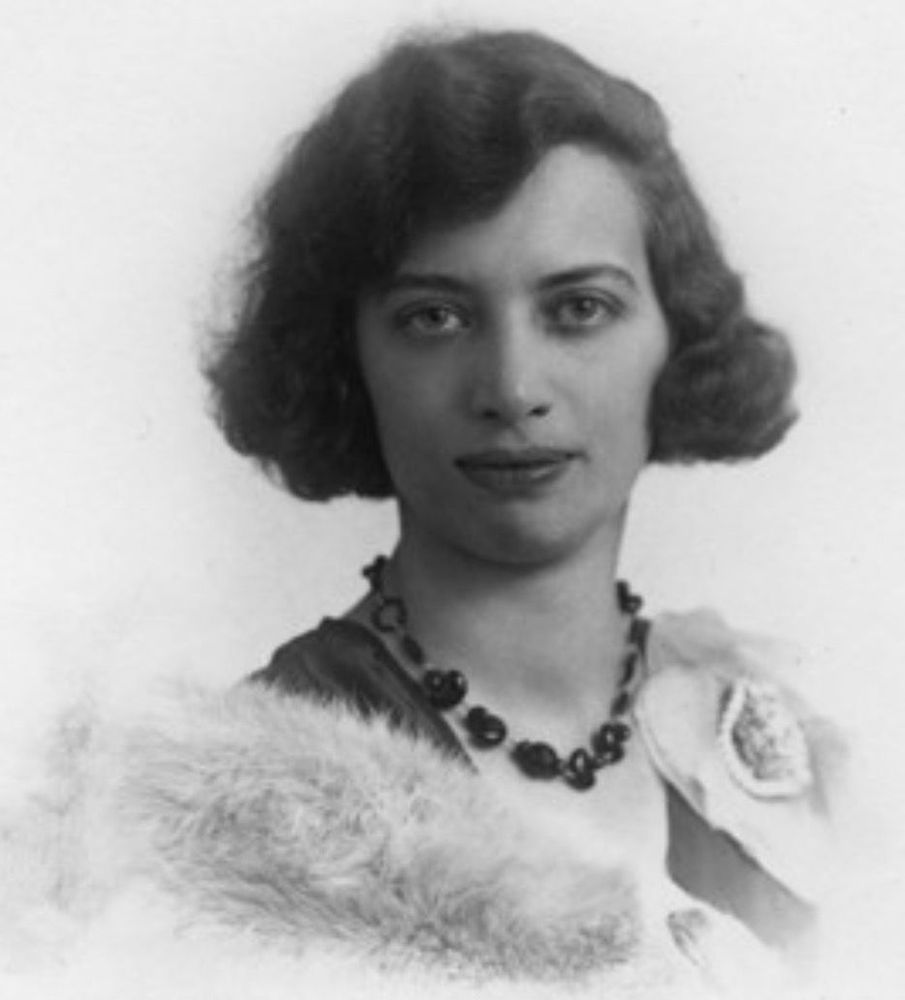 Black and white portrait of a woman with medium-length hair wearing a necklace and a fur stole, displaying a soft smile.