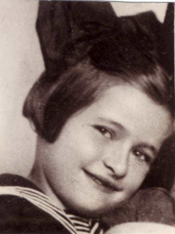 Vintage black-and-white photo of a smiling young girl wearing a large bow in her hair and a striped outfit.