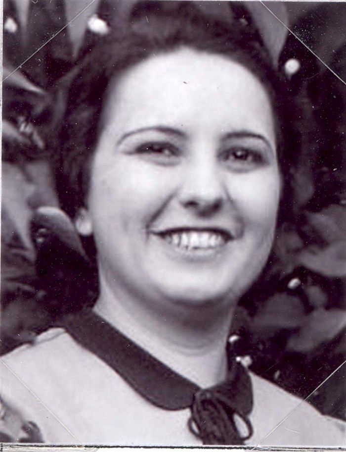 Black and white photo of a smiling woman with short hair, wearing a necklace, set against a leafy background.