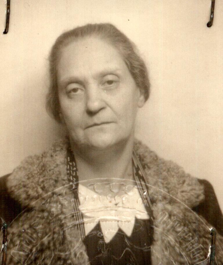 Vintage black-and-white portrait of an elderly individual wearing a fur coat and a decorative blouse, displaying a solemn expression.