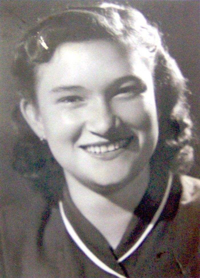 Vintage black-and-white portrait of a smiling woman wearing a light-collar shirt and a dark jacket.