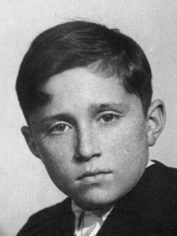 A black and white headshot of a young boy, showing him looking directly at the camera with a neutral expression. He has short hair.