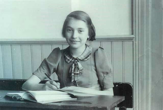 Photograph of teenage girl sitting at a desk, smiling slightly while writing in a notebook.