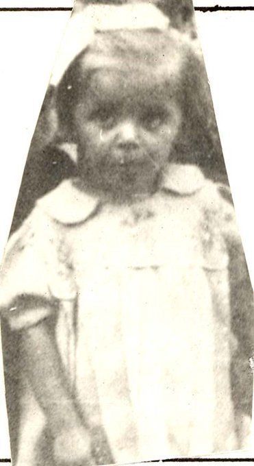 Old sepia-toned photograph of a young child standing outdoors,