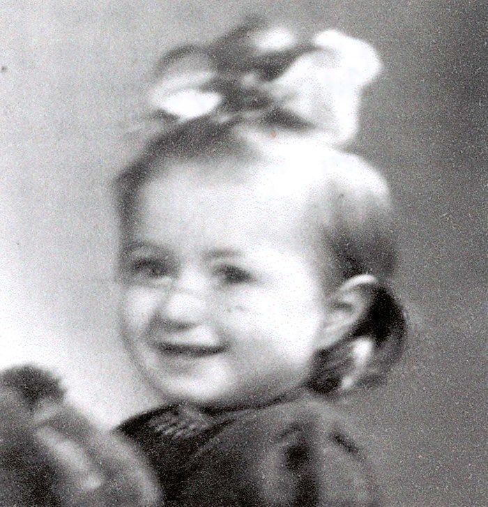 This image features a close-up of a smiling young girl with short hair styled with a large bow on the top. The girl is wearing a dark coat.