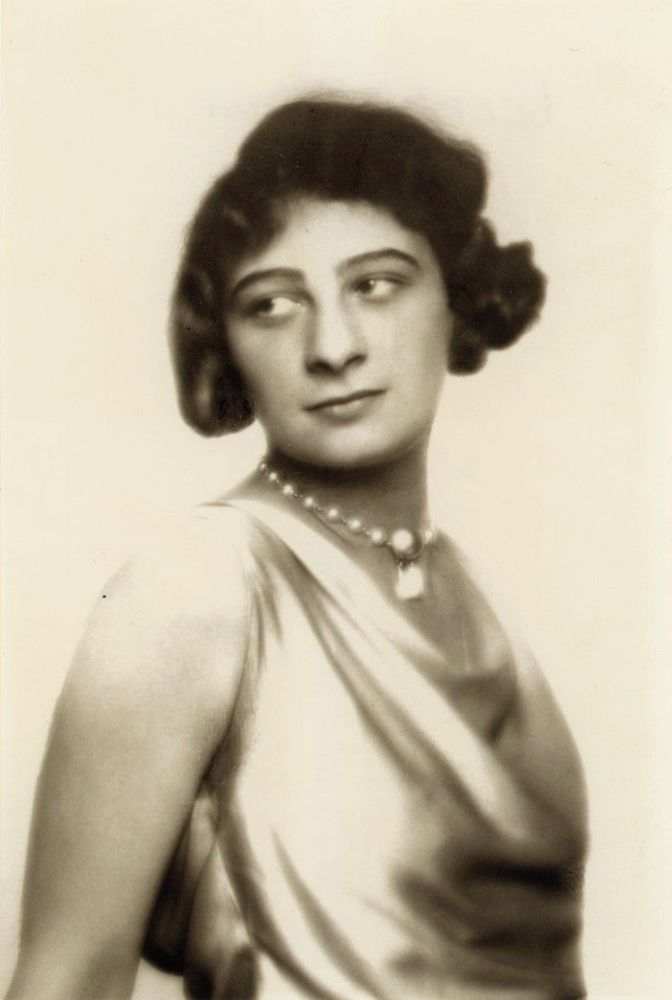 Vintage black-and-white portrait of a woman in an elegant gown with a pearl necklace, showcasing a formal and poised appearance from an earlier era.