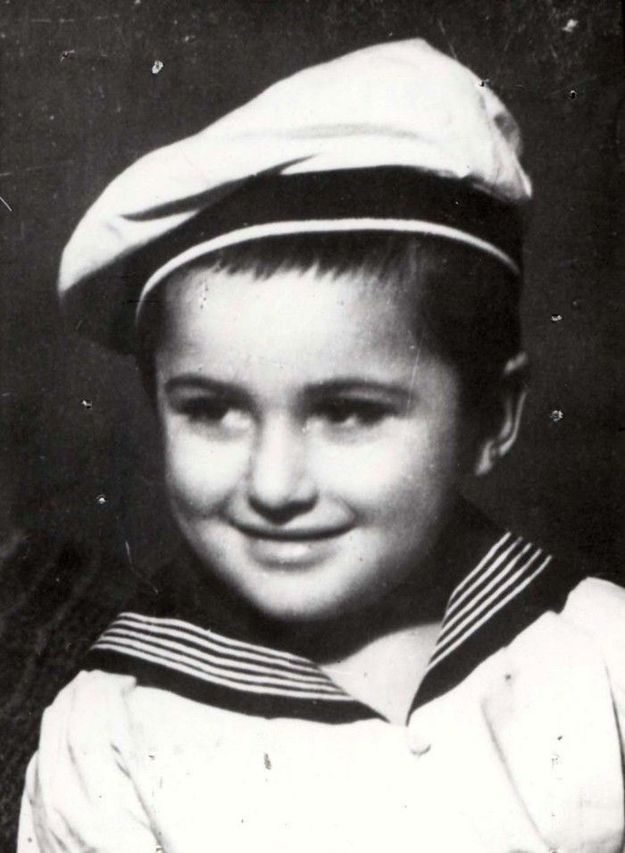 Black and white photo of a boy in a sailor outfit, featuring a striped top and sailor cap. The child is smiling and looking slightly to the left of the frame.