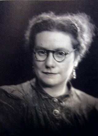 Vintage black-and-white portrait of a woman wearing glasses and a high-collared blouse, exuding a formal and reflective atmosphere.