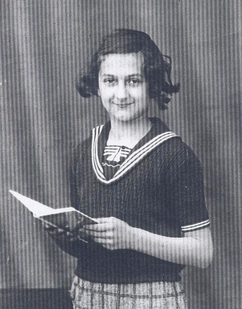 A photo of a girl holding a book. She is wearing a short sleeved blouse and checked dress.