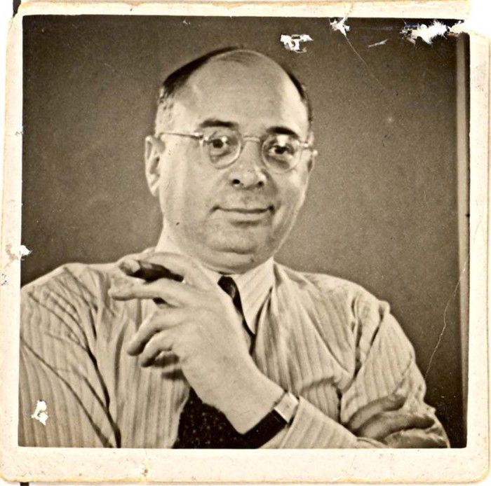 Vintage portrait of a man wearing glasses and a striped shirt, posing with one hand on their cheek.
