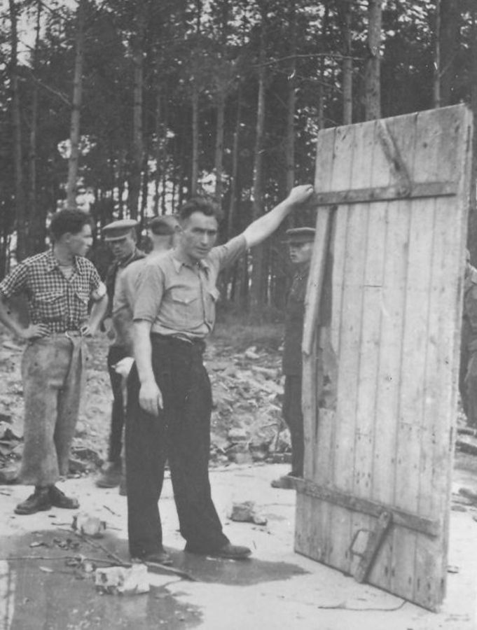 Some people in a wooded area examining a large, wooden gas-tighed door - remains of gas chamber and crematorium V at the former Auschwitz II-Birkenau site.