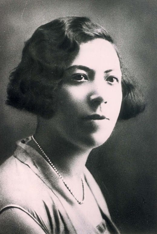 Black and white portrait of a woman with short curly hair, wearing a light-colored outfit and a delicate necklace.