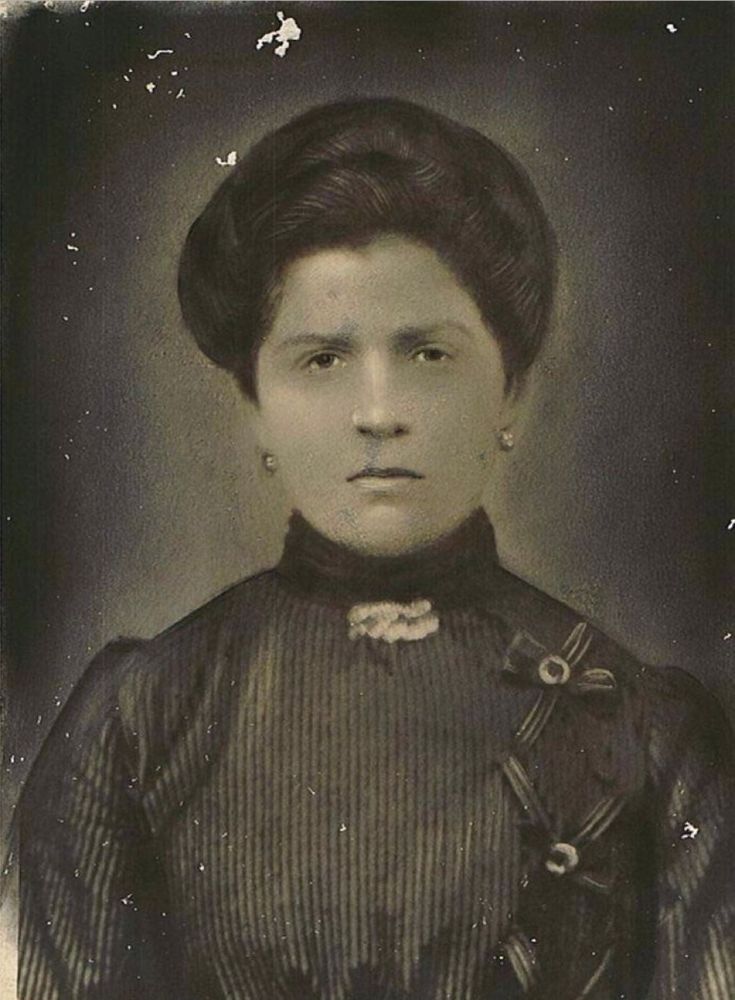 A portrait photo of a mature woman. You can see she is wearing a dark dress that also covers her neck.