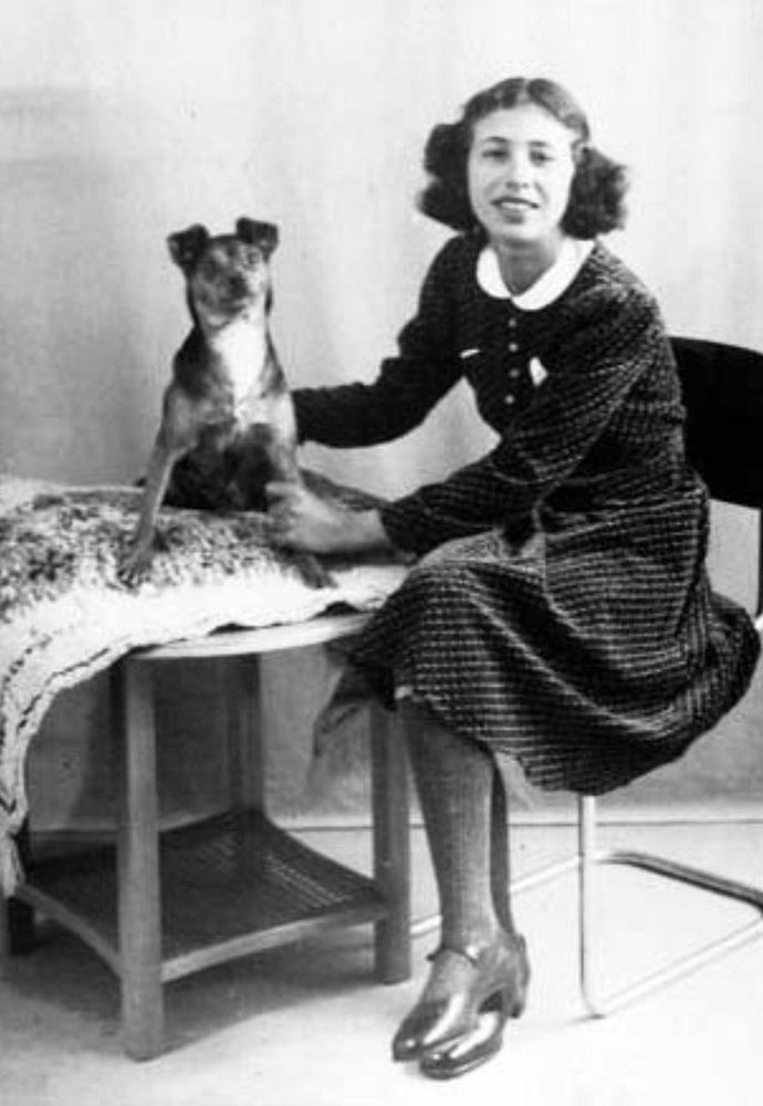 Vintage black and white photo of a woman seated beside a small dog on a table, gently touching it.