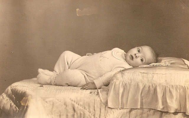A baby boy lying on a bed and a pillow.