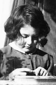 A black and white photo of a young girl focusing on something she is holding in her hands. She is pictured with her head bowed slightly towards, displaying a concentrated expression. The setting appears to be indoors, with light coming from the side, partially illuminating her face and her writing desk.