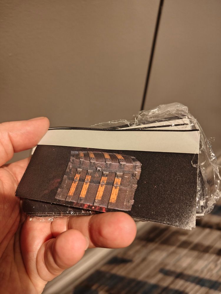 My hand holding a pile of con ribbons. Pictured is a full-color image of a trunk overlaid against a red-black starry background.