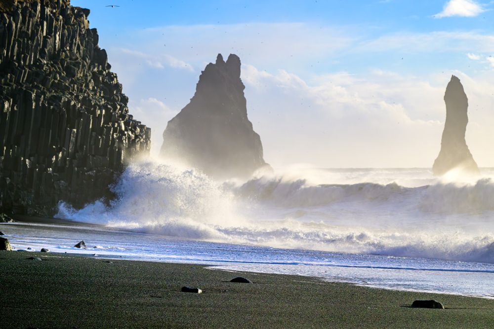 Waves crashing onto a black sand beach by the Tetris Cave