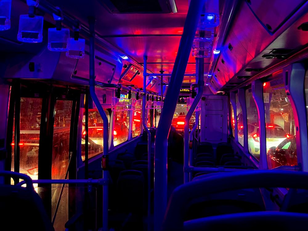 Nighttime bus interior glowing with blue and red lights amidst city traffic