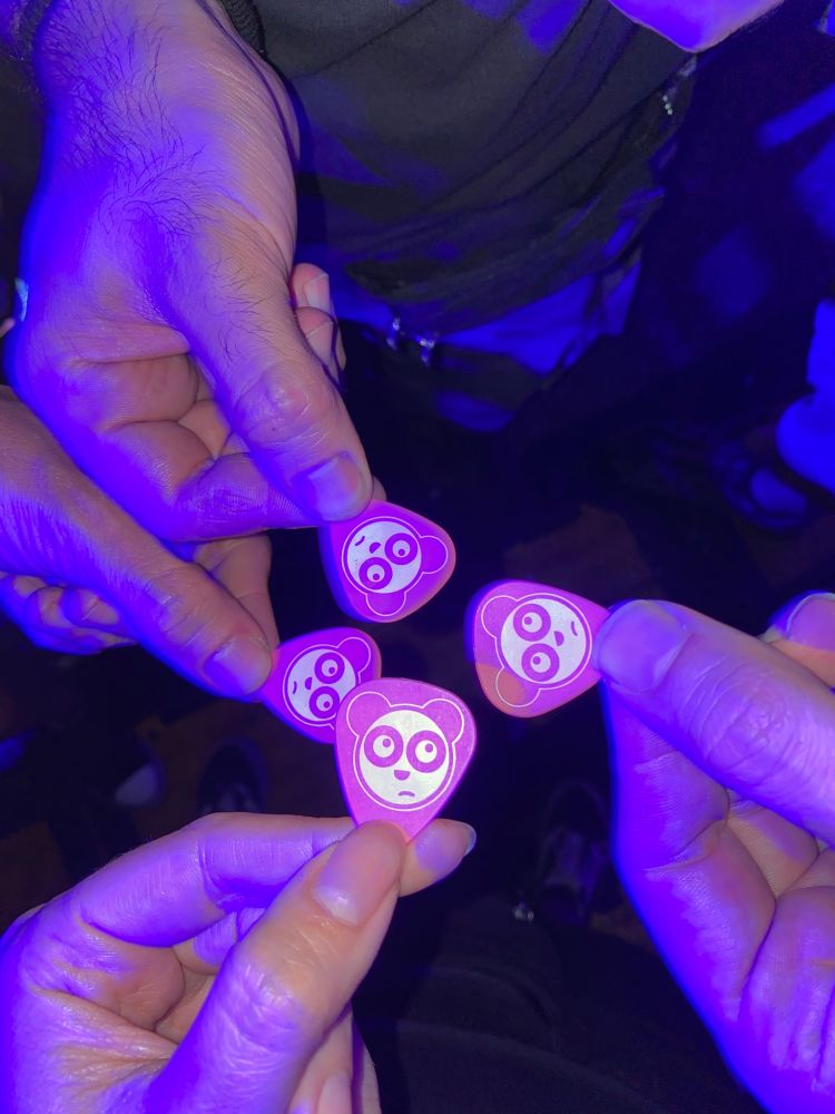 Foto de cuatro manos sujetando cuatro púas rosas en la que está grabado el dibujo del oso panda de lendakaris muertos