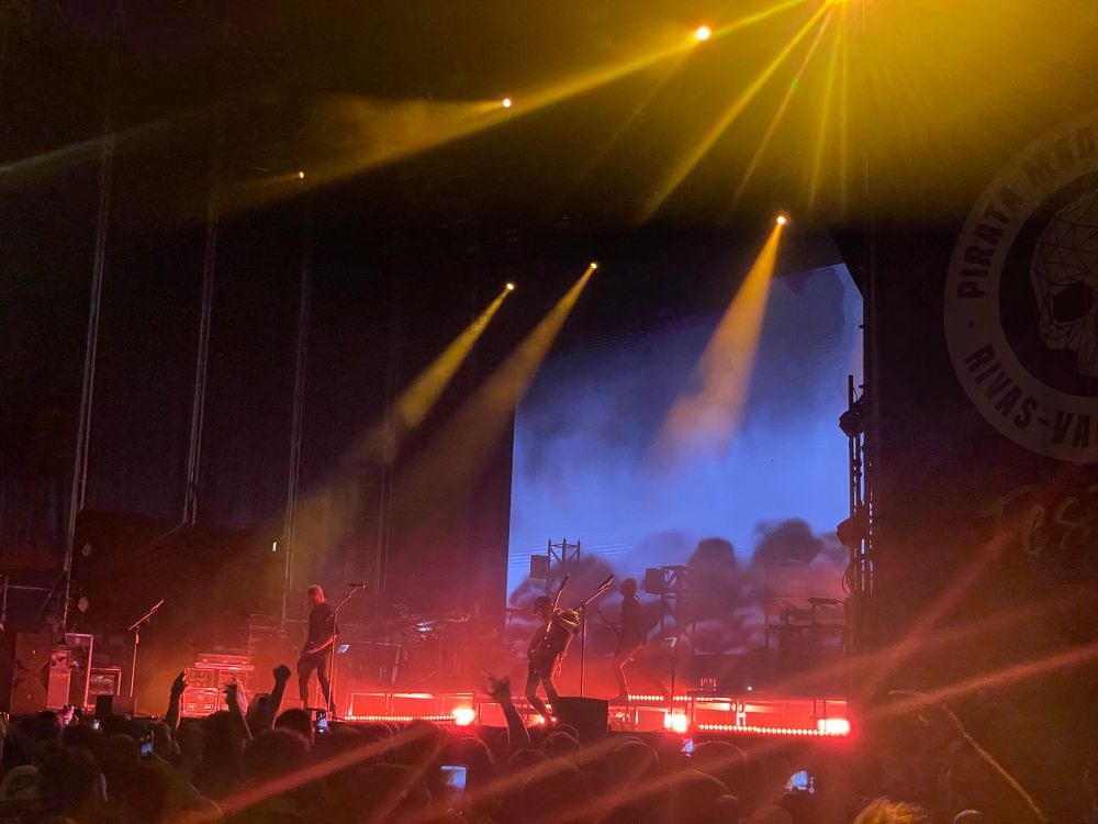 Concierto de Pendulum. Tienen luz trasera, floja, anaranjada. Una pantalla con imagen en azul. Se ve ligeramente a los artistas.