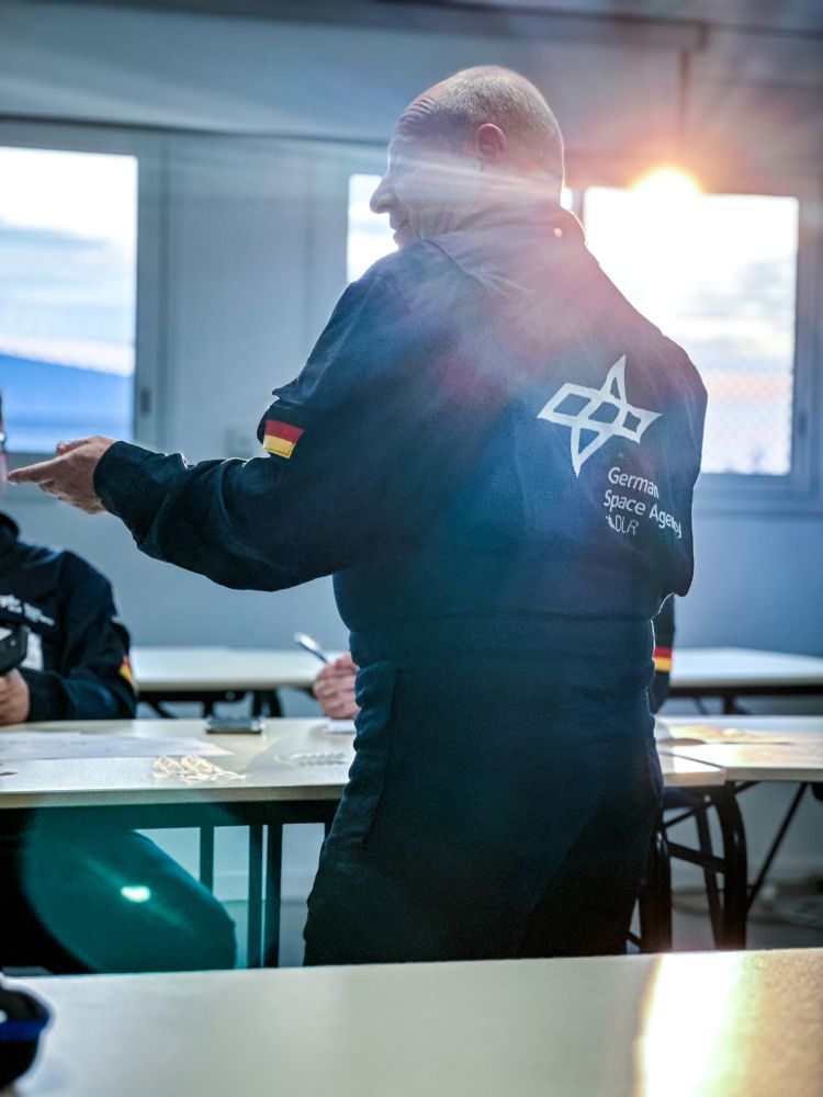 Researcher standing wearing a DLR flight suit in a briefing with his team. 