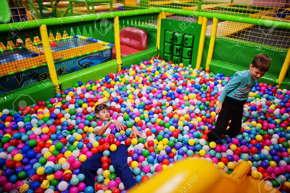 Two children playing in a ball room full of colorful balls 