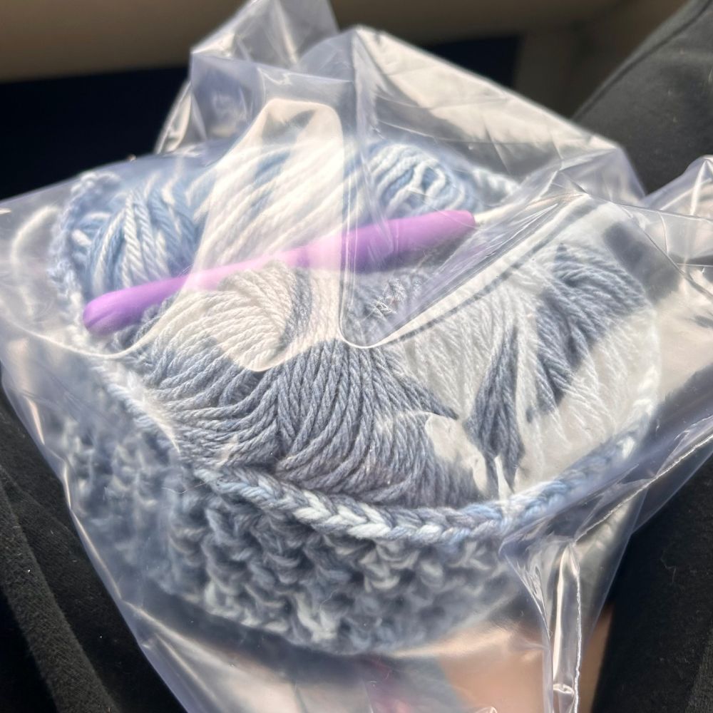 A clear plastic bag containing an unfinished crochet basket containing yarn and a crochet hook.
