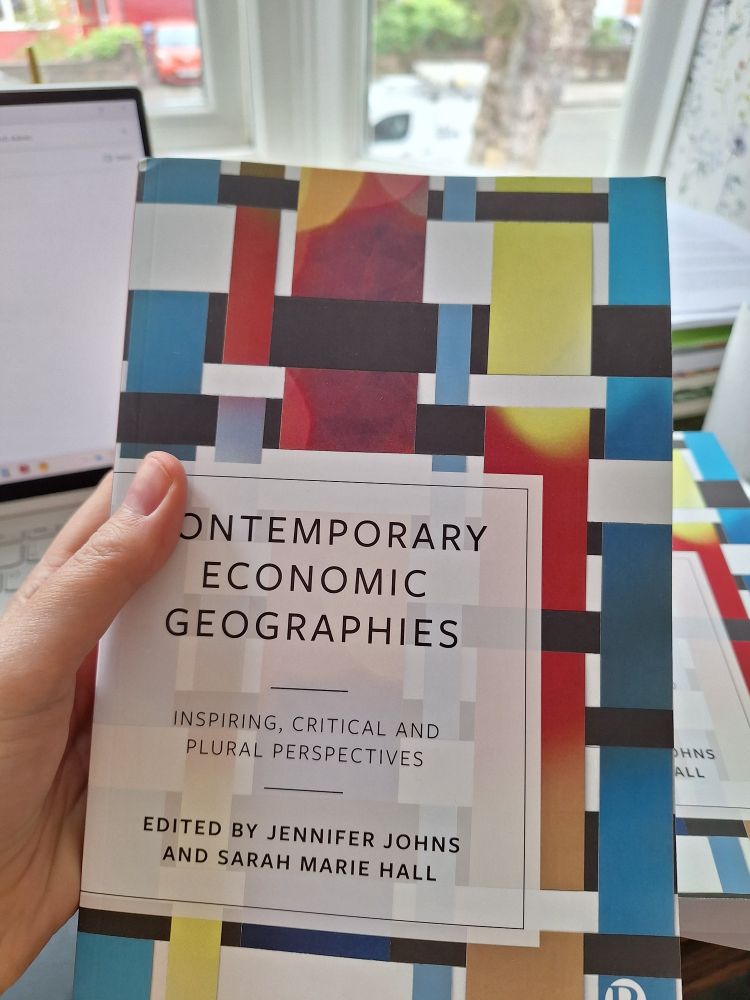 Sarah's hand holding a copy of the co-edited book 'Contemporary Economic Geographies' in paperback. With Jennifer Johns.