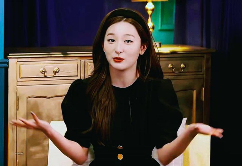 a woman wearing a black dress and a headband is sitting in front of a dresser