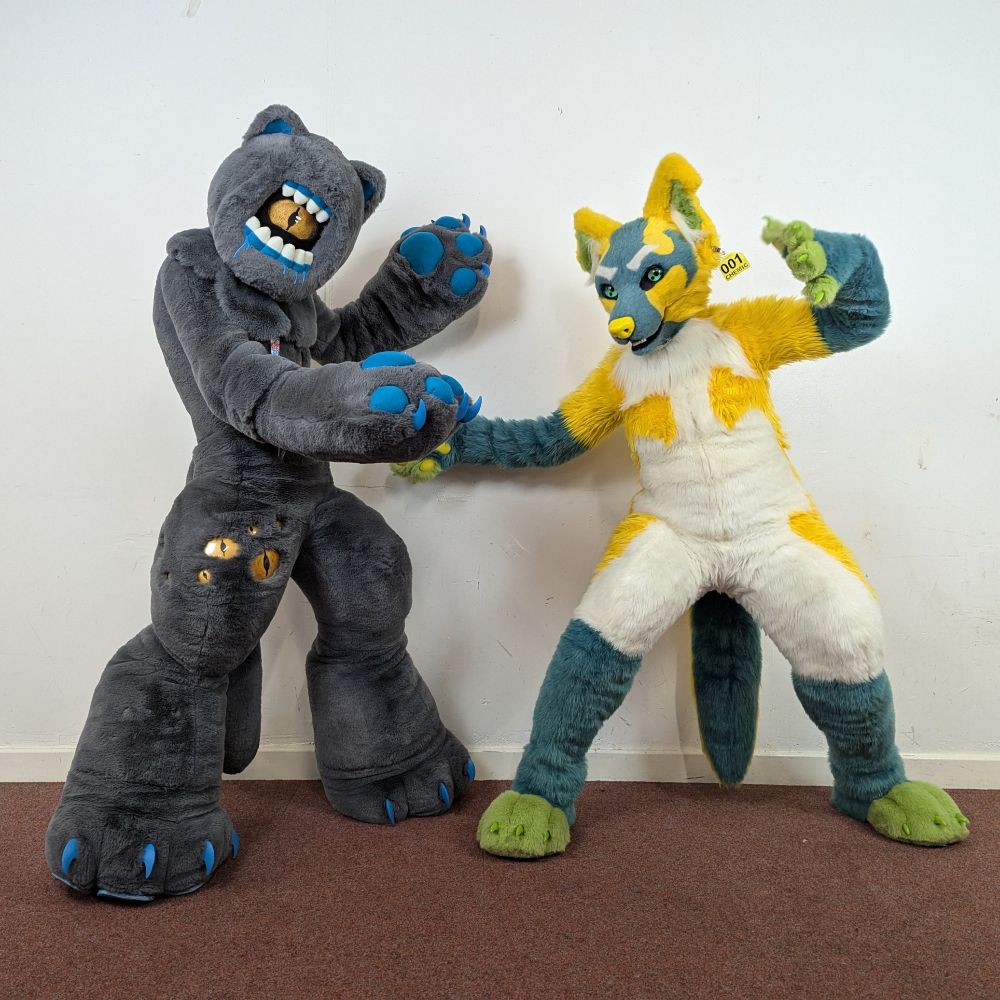 Two fursuiters posing. On the left is a grey alien cat with a 'mouth eye', and on the right a toxic waste themed yellow/green/blue canine.