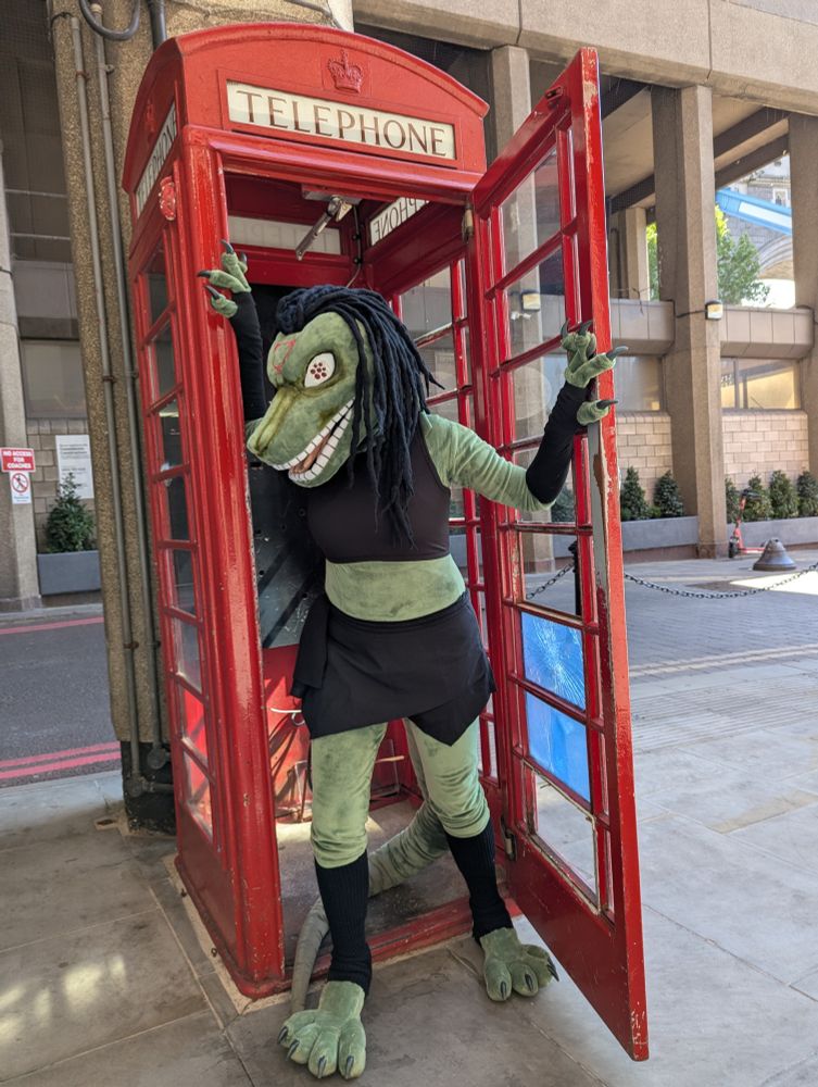 Photo of me cosplaying as an anthro version of Envy's true/monster form - a character from Full Metal Alchemist. the photo recreates a scene from the anime where Envy shoots and kills Maes Hughes in a public telephone box.