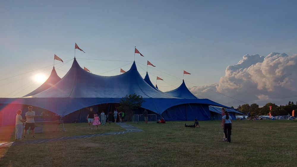 Photograph of the big top tent at a festival with the sun setting behind it. 