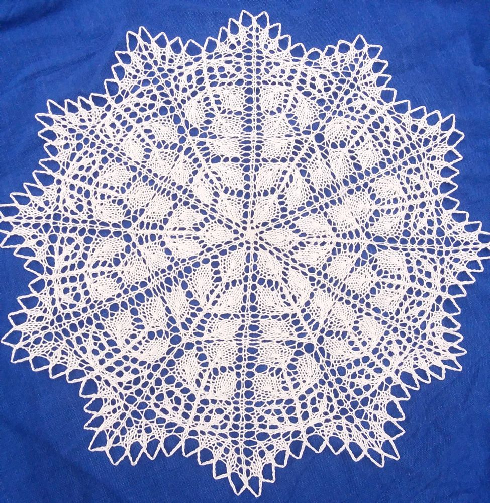 Knitted white cotton doily with 12-fold circular symmetry repeating a diamond-shaped leaf-like pattern