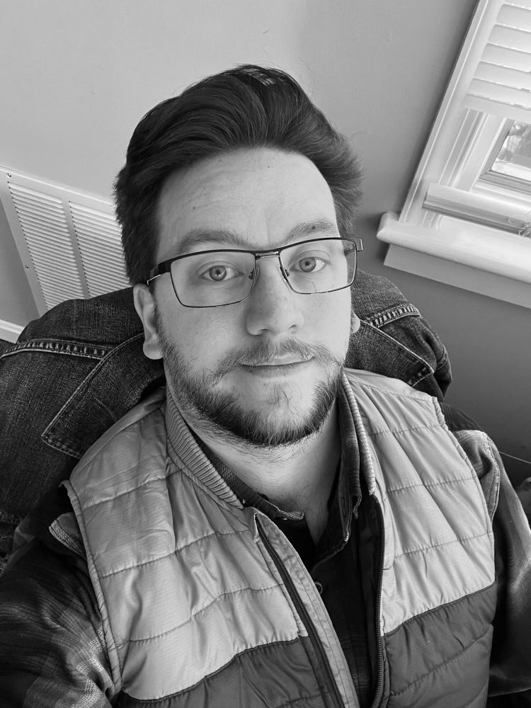 Black and white selfie of me looking slightly up at my phone camera in my work office