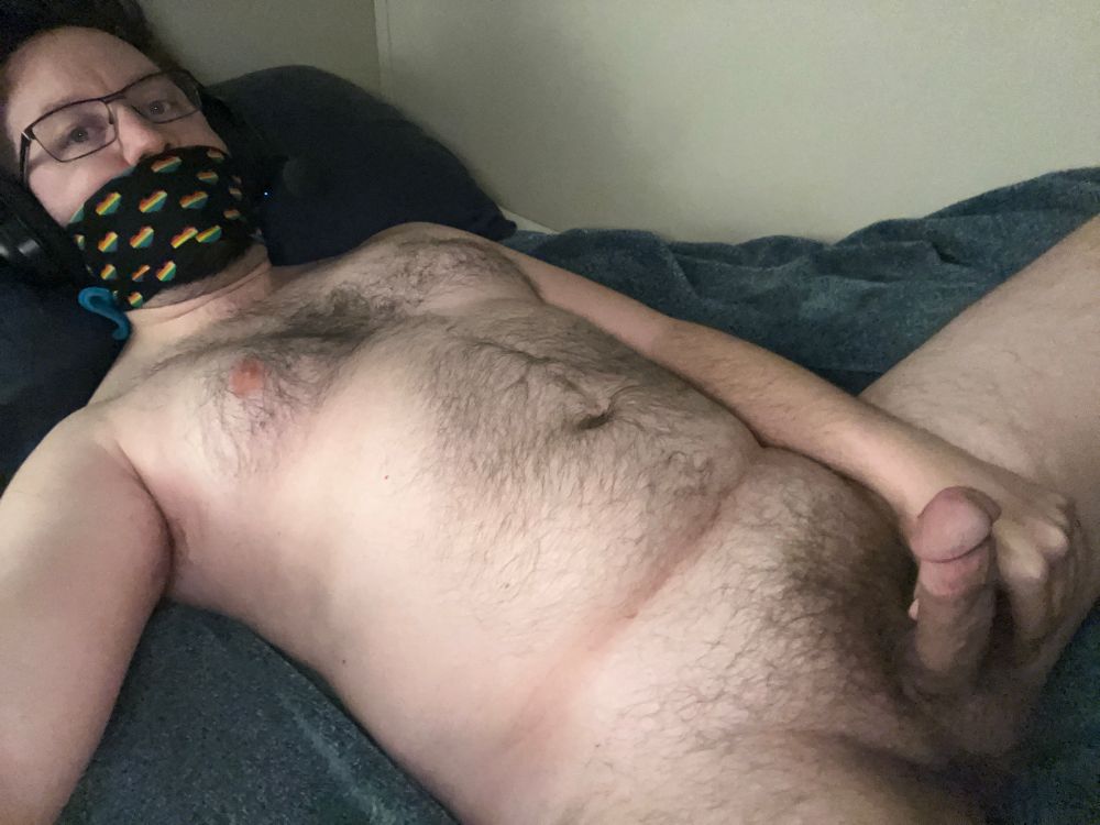 Me laying naked in bed, penis fully erect. I’m wearing only my glasses, gaming headphones w/ mic, with a long sock and bandana tied snugly over my mouth to keep me quiet as I masterbate